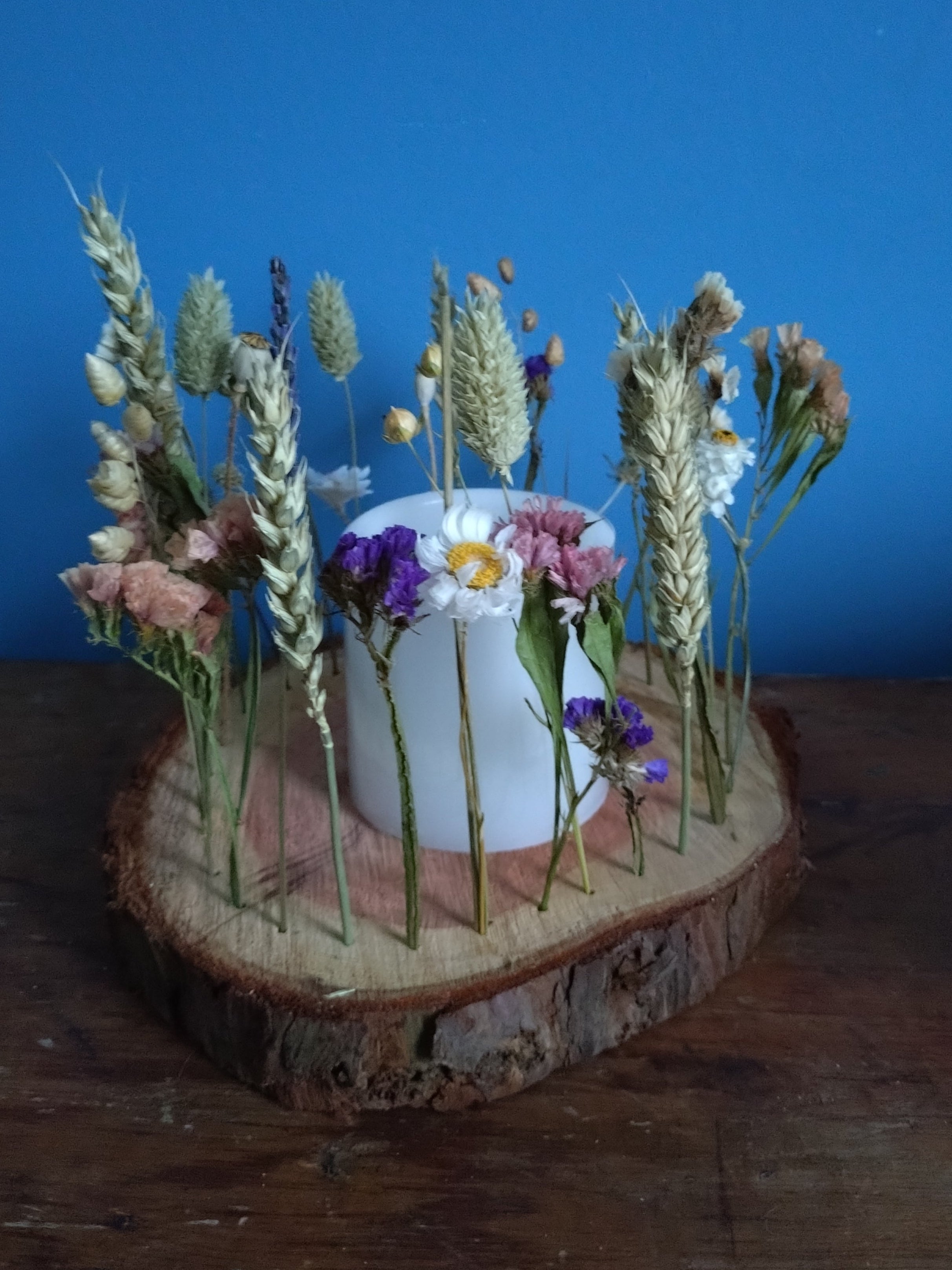 Decorative arrangement of flowers and a candle on a wooden log against a blue background