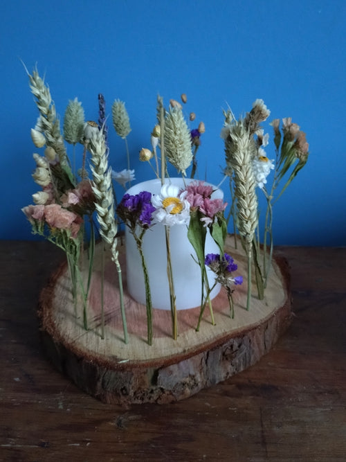 Decorative arrangement of flowers and a candle on a wooden log against a blue background