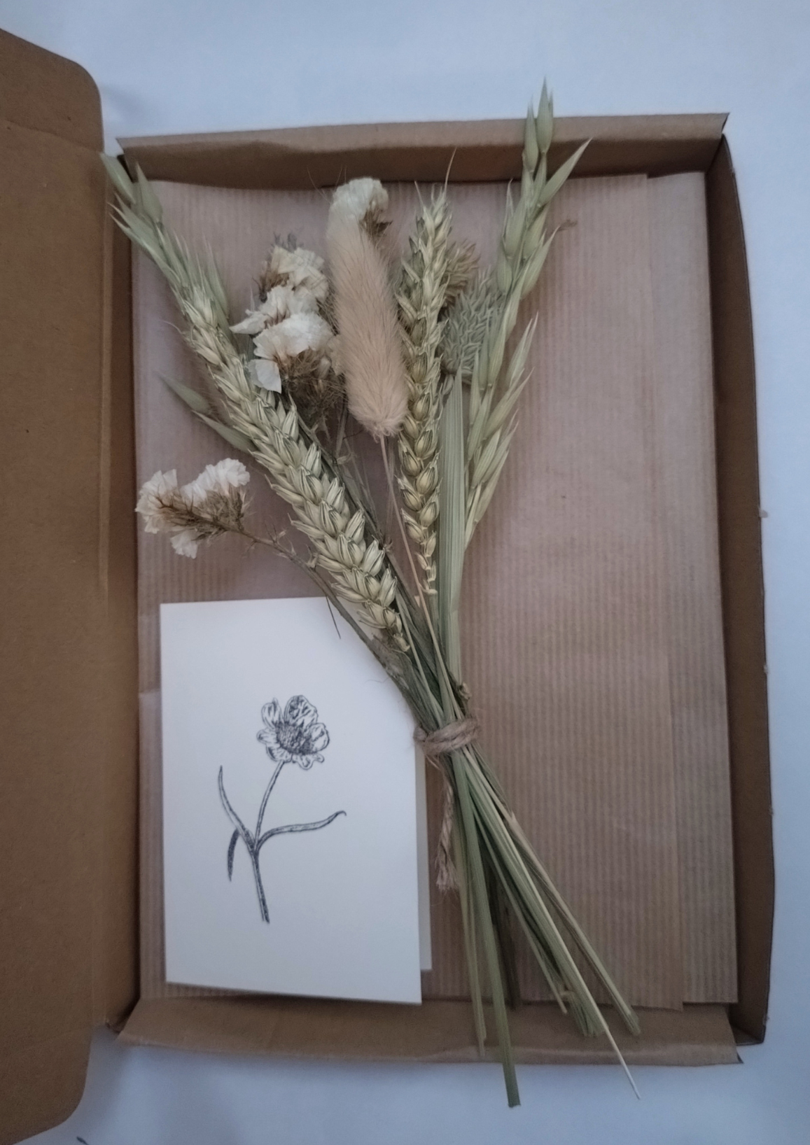 Bouquet of dried flowers and a card inside an open brown box on a white background